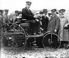 Carl Benz auf seinem ersten Patent-Motorwagen vom Typ I aus dem Jahr 1886, aufgenommen in München im Jahr 1925.